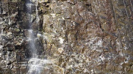 Wall Mural - Little waterfall in rocky mountains near the parking at Ornesvingen viewpoint, Geiranger, Norway. Water falling in slow motion.