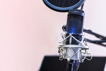 Condenser microphone on holder and pop filter with blue light swith on for voice over on blurred monitor background and copy space