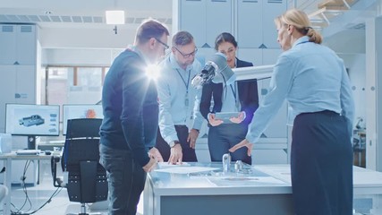 Leinwandbilder - Diverse Team of Industrial Robotics Engineers Gathered Around Table With Robot Arm, They Use Tablet Computer to Manipulate and Program it to Pick Up and Move Metal Component. Bright Facility
