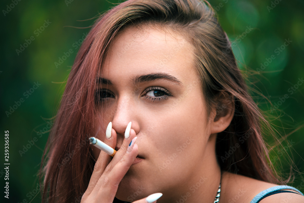 Portrait of a young pretty girl with red hair smoking a cigarette. Stock  Photo