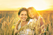 © sborisov - Young woman and her daughter on golden wheat field at sunny summer evening.