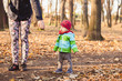 © pawczar - A young mom on a walk in the park with her one year old son. The woman wants her child to give her a hand. Motherhood is a happy time for the whole family. The boy just learned to walk.