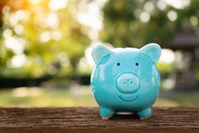 Blue Piggy Bank On Wooden Table Over Blurred Green Bokeh Background. Saving Money Concept
