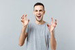 Portrait of funny young man in casual clothes shouting, growling like animal, making cat claws gesture isolated on grey wall background. People sincere emotions, lifestyle concept. Mock up copy space.