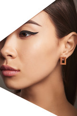Wall Mural - Cropped side half-turn geometric portrait of Korean girl with plush lips and black flicks. The lady is wearing a brown rectangle-shaped earring, looking directly behind triangle-shaped foreground.