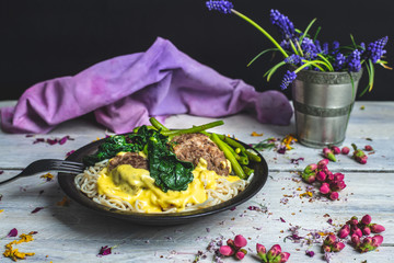 in a bright, rustic kitchen, on a wooden table lies a plate of spaghetti with cheese sauce, garlic, meatballs, spinach and green bean stew