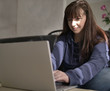 © OlgaVELES - Young pretty brunette smiles while typing on laptop