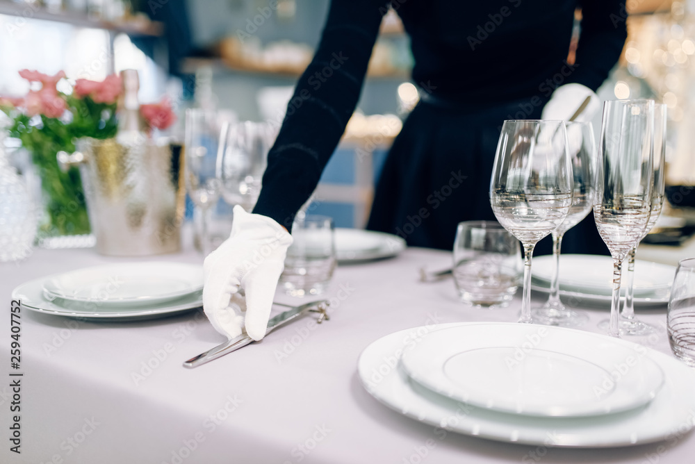 Waitress in gloves puts the knife, table setting - obrazy, fototapety, plakaty 