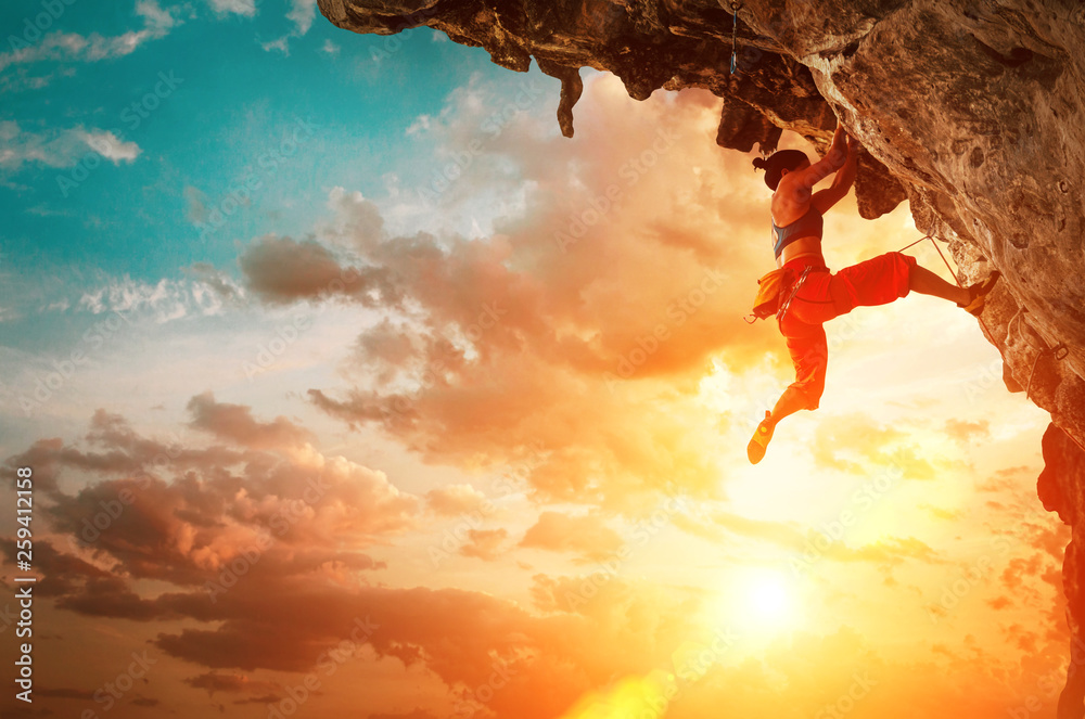 Athletic Woman climbing on overhanging cliff rock with sunset sky background - obrazy, fototapety, plakaty 