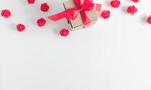 Gift With Red Satin Bow And Red Artificial Flowers On White Background. Flat Lay, Top View, Copy Space