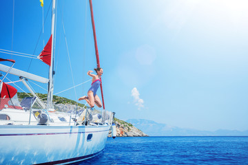 Girl jump in sea of sailing yacht on summer cruise. Travel adventure, yachting with child on vacation.