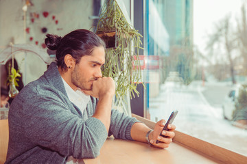 Young man watching smartphone and biting fist in worried expression.
