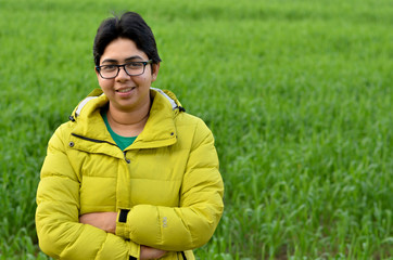 Wall Mural - Happy looking smiling Indian woman wearing spectacles standing in a farm against green crops in an Indian village