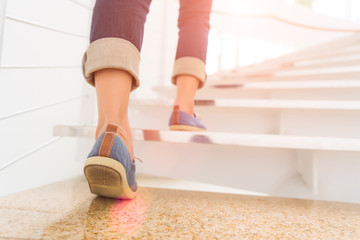 Wall Mural - young adult woman walking up the stairs with sun sport background.