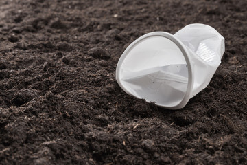 Crumpled, non-extinguishing plastic cup on black soil. Environmental concept. Pollution by plastic waste.