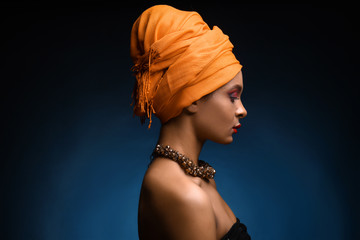 Portrait of beautiful African-American woman with head scarf on dark color background