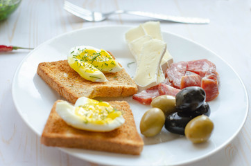 Simple breakfast on white background. Eggs, toast, olive, salami, cheese