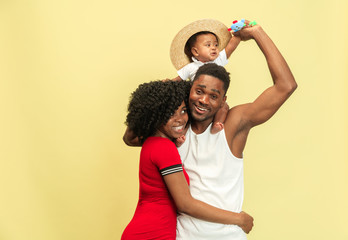 Wonderful moments together. Happy african american family with little child on yellow studio background. Leisure, togetherness, relationship, childhood and human emotions concept.