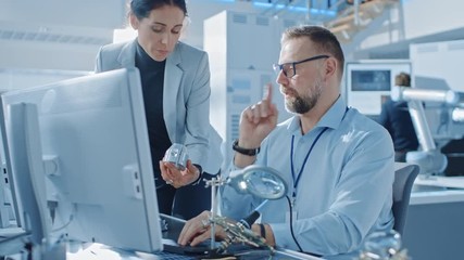 Leinwandbilder - Female Industrial Engineer Talks with Electronics Specialist, She Holds Metal Component Prototype, he Works on Computer. Modern and Bright Office with Stylish People 