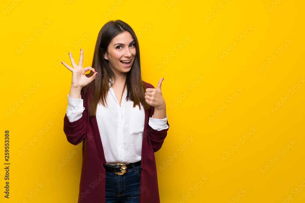 Young woman over yellow wall showing ok sign with and giving a thumb up gesture - obrazy, fototapety, plakaty 