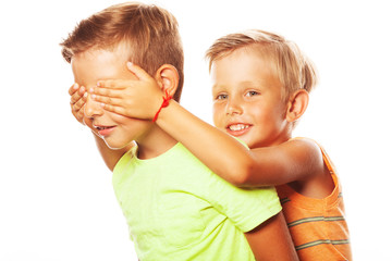 Guess Who, See no evil concept. Two funny siblings brothers playing hide-and-seek game: younger boy embraces face of his elder friend. Older one is intrigued. Close up. Studio shot