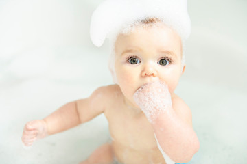 A Baby girl bathes in a bath with foam and soap bubbles