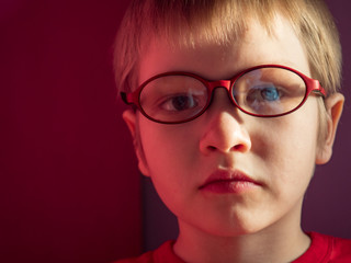 Wall Mural - Funny child in red sweater on red background actively expresses emotions. Close up little kid boy in glasses posing front of camera