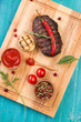 © yakovlevadaria - Steak on a cutting board, sauce and pepper, blue wooden background, top view