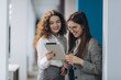 © JJ Studio - Two female managing directors discussing ideas of project on digital tablet while walking down in office hall, confident women entrepreneurs working on touch pad while going to the conference room