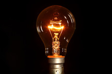 Clear Glass Electric Lightbulb Dimmed To Enable It's Tungsten Filament To Be Seen Isolated On A Black Background