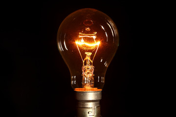 Clear glass electric lightbulb dimmed to enable it's tungsten filament to be seen isolated on a black background