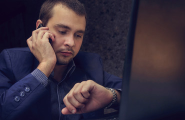 Young businessman looks at the time on the clock, talking on the phone.