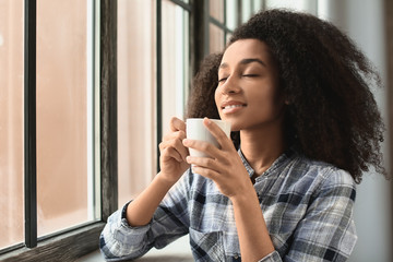 Wall Mural - Beautiful African-American woman drinking coffee near window