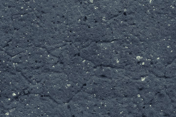 Uneven surface of dark gray concrete wall close-up. Rough texture of grey cement wall with small white stones. Dark asphalt texture.