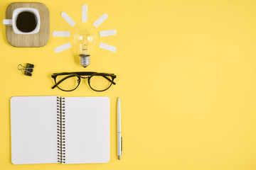 Top view flat lay of workspace desk styled design office supplies with pen, notepad, eyeglasses, cup coffee and light bulb on a yellow color paper background minimal style. Concept brainstorming