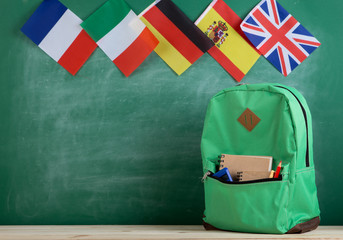 Fototapete - backpack, flags of Spain, France, Great Britain and other countries and school supplies on the background of the blackboard