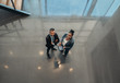 © JonoErasmus - Two business people standing in the lobby of an office looking up smiling at the camera while