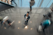 © JonoErasmus - Black african business woman standing in the lobby of an airport looking up at the camera while people are walking past in a blur