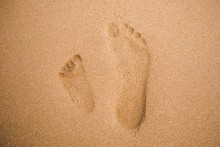 Child And Adult Footprints On Sand Beach