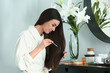 Beautiful young woman applying serum onto her healthy long hair at home