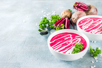 Spring vegetable soup. Homemade beet cream soup, with fresh organic beetroot, sour cream and herbs, blue concrete background copy space