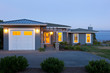 © ML Harris - Contemporary house and garage at dusk with exterior lighting and lights on inside. Home energy use, water view real estate.