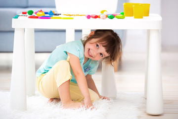 Little cute girl crawled under the table. The kid smiles, plays hide and seek