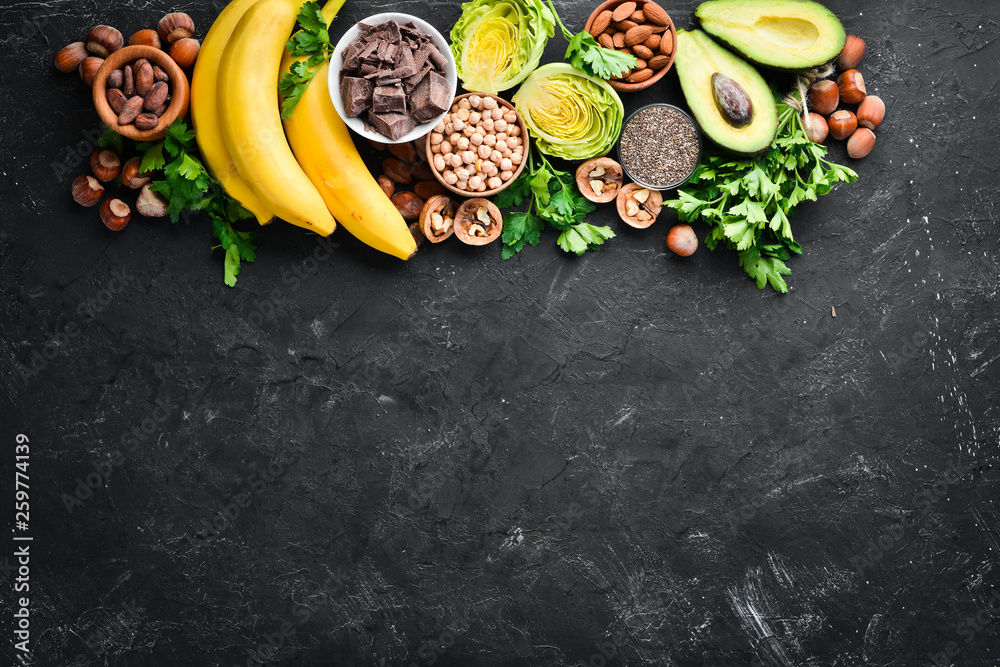Foods containing natural magnesium. Mg: Chocolate, banana, cocoa, nuts, avocados, broccoli, almonds. Top view. On a black background. - obrazy, fototapety, plakaty 