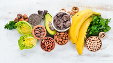 Foods Containing Natural Magnesium. Mg: Chocolate, Banana, Cocoa, Nuts, Avocados, Broccoli, Almonds. Top View. On A White Wooden Background.