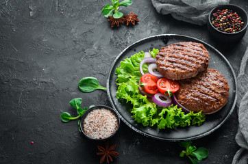 fried cutlet for burger with vegetables. In a black plate on a wooden background Top view. Free space for your text. Flat lay