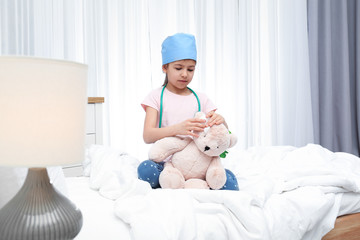 Wall Mural - Cute child playing doctor with stuffed toy on bed in hospital ward