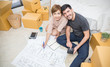 © paulaphoto - Asian woman and caucasian man carry boxes sitting on the floor planing for decorating with pile of blue print plan paper boxes. Moving house just married diversity interracial  couple concept.