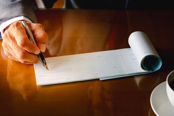 Wall Mural - Business man hand writing and signing checkbook on the wooden table at office. Paycheck or payment by cheque concept.	