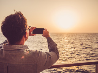 Trendy man holding a mobile phone on the empty deck of a cruise liner against the backdrop of the sea waves. Side view, close-up. Concept of technology, recreation and travel